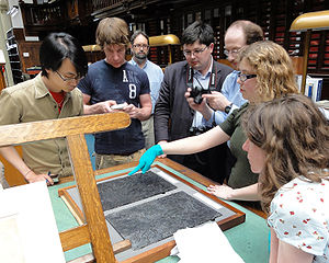 Photograph of students gathered around a museum keeper, who is showing them a Dürer print block made of pear wood